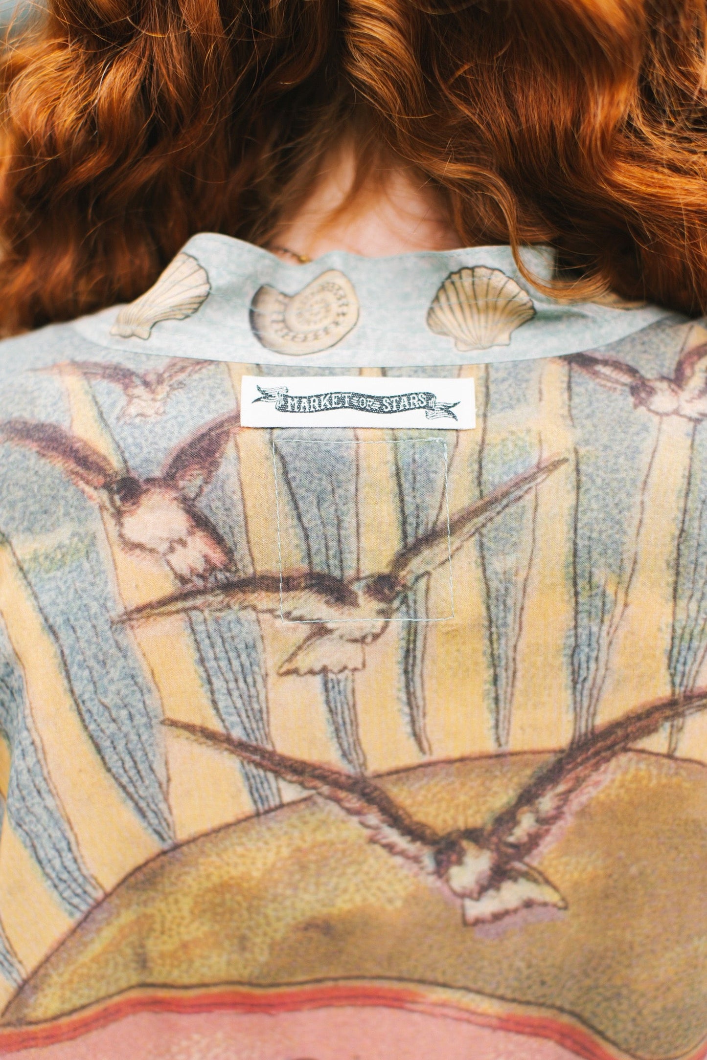 Lightweight duster featuring antique sunrise sky, mermaid, shell, and soaring birds artwork, shown on model at the beach – Market of Stars