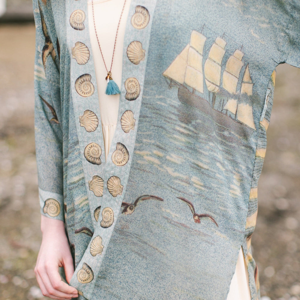 
                  
                    Lightweight duster featuring antique sunrise sky, mermaid, shell, and soaring birds artwork, shown on model at the beach – Market of Stars
                  
                