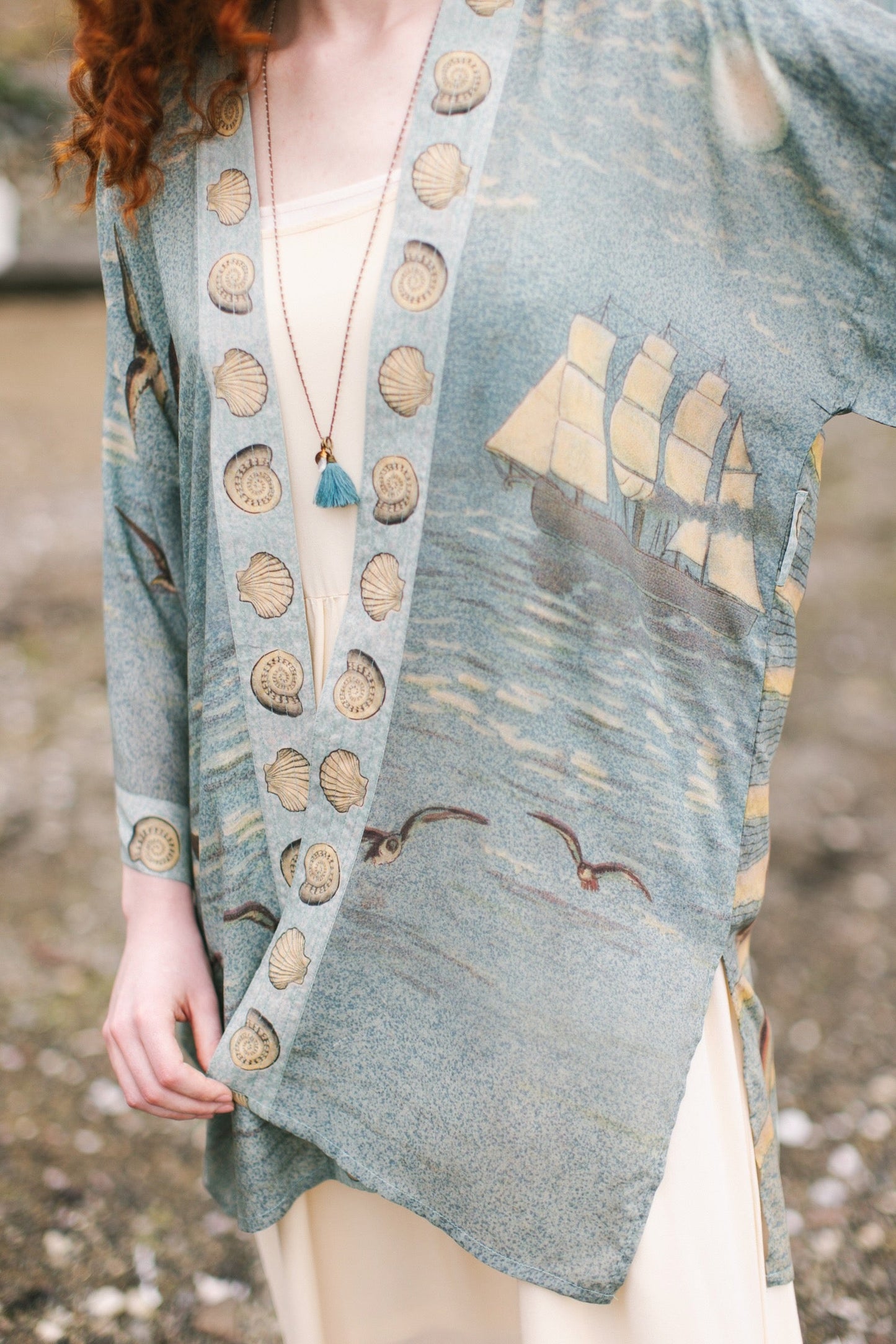 Lightweight duster featuring antique sunrise sky, mermaid, shell, and soaring birds artwork, shown on model at the beach – Market of Stars