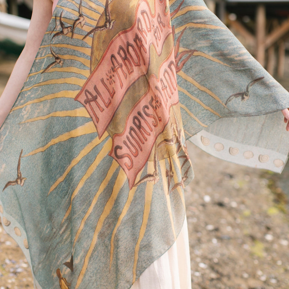 
                  
                    Lightweight scarf featuring a dreamy sunrise landscape and nautical artwork with the words "All aboard for Sunrise Lands" – Market of Stars
                  
                