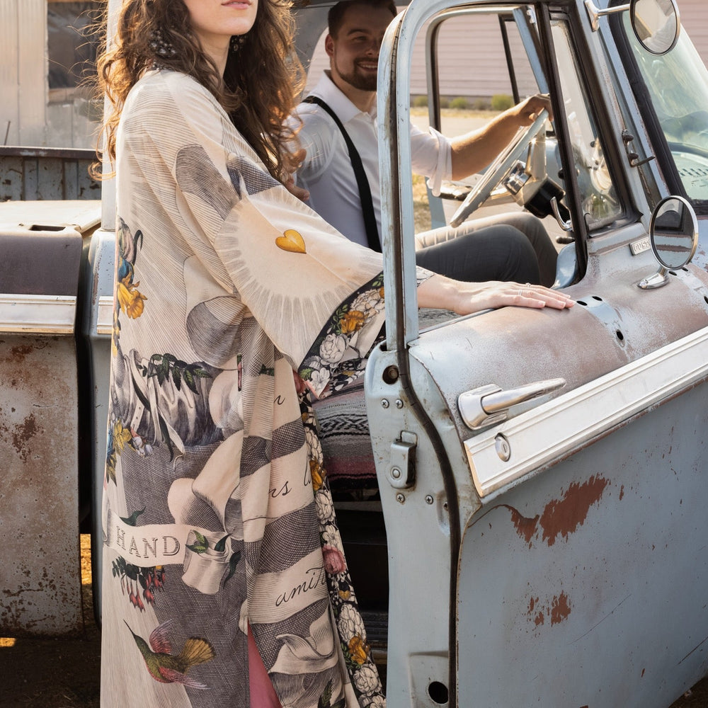 
                  
                    Clasped hands, radiant sun rays, and blooming florals in a joyful Victorian collage on our full-length Take My Hand Opera Duster
                  
                