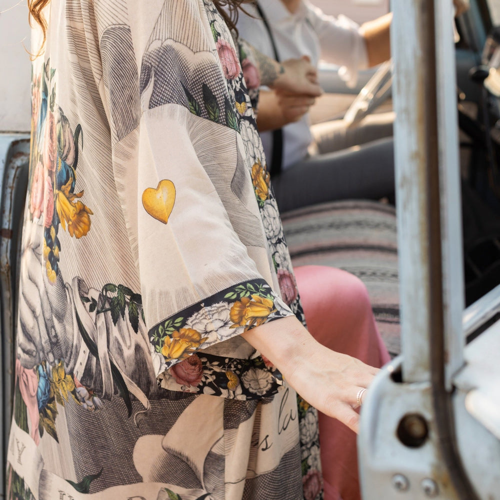 
                  
                    Clasped hands, radiant sun rays, and blooming florals in a joyful Victorian collage on our full-length Take My Hand Opera Duster
                  
                