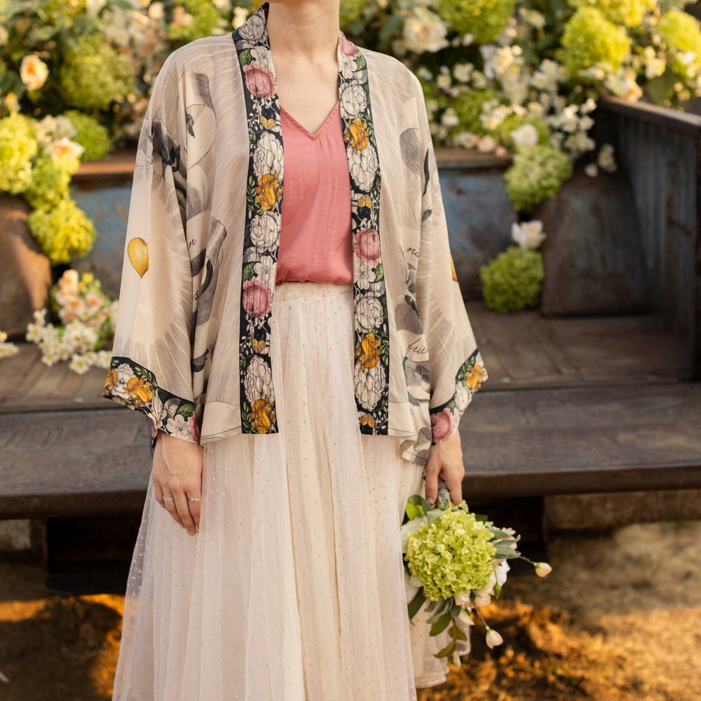 
                  
                    A joyful blend of 17th-century engravings, painted hearts, and hand-coloured florals on our cropped Take My Hand Pixie duster kimono – Market of Stars
                  
                