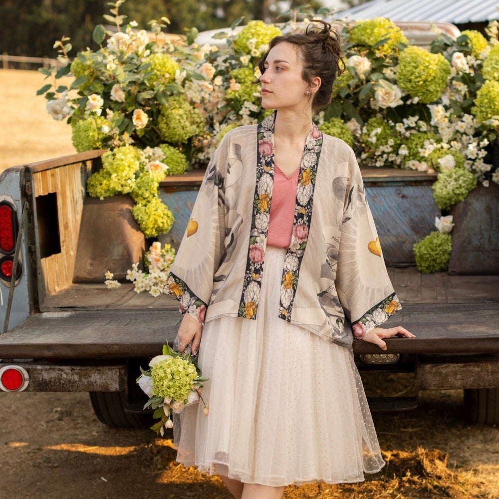 
                  
                    A joyful blend of 17th-century engravings, painted hearts, and hand-coloured florals on our cropped Take My Hand Pixie duster kimono – Market of Stars
                  
                