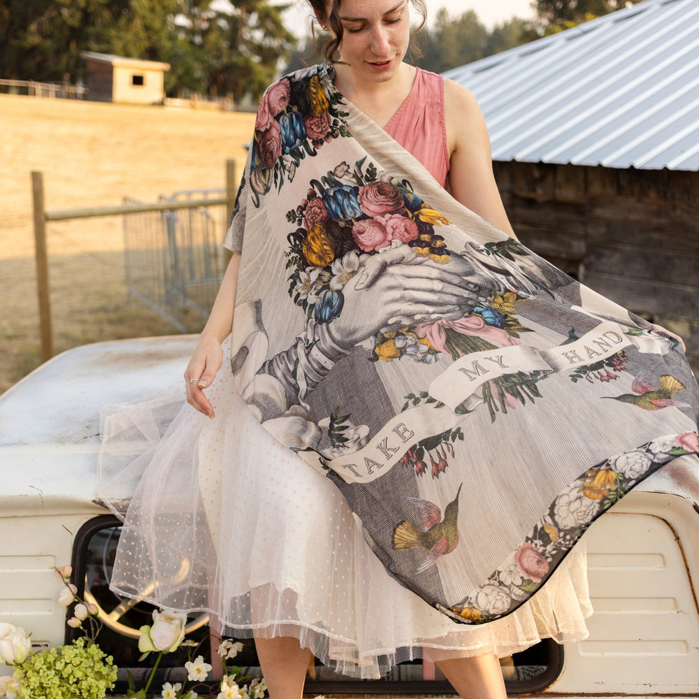 
                  
                    Model wearing Take My Hand scarf with 1600s hand engraving of clasped hands, a painted heart, florals and sun rays – Market of Stars
                  
                