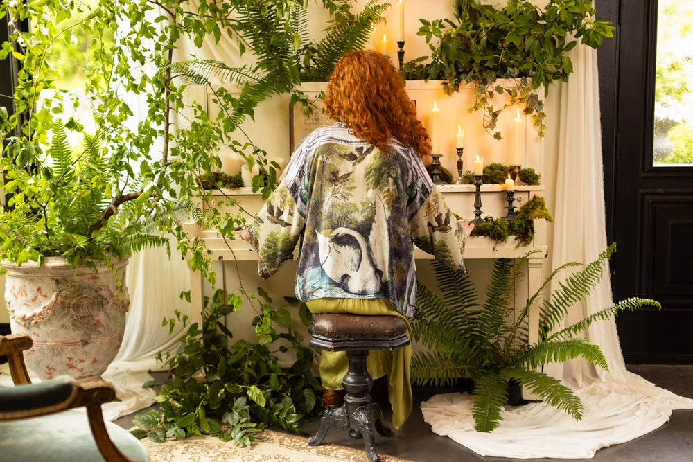 
                  
                    Model wearing the cropped Theatre of Dreams kimono featuring painted swan, antique script, and whimsical theatre imagery from artist Jennifer Lanne
                  
                