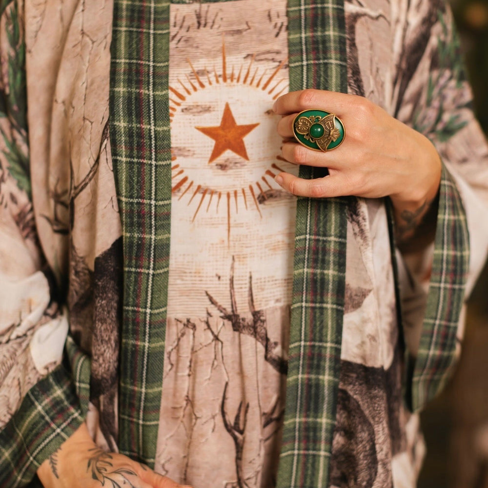
                  
                    Model wearing a bamboo viscose mid-length duster with Victorian-era images from holiday greeting cards — including reindeer in the snow, a little fir tree, golden stars, and traditional plaid trim - Market of Stars
                  
                