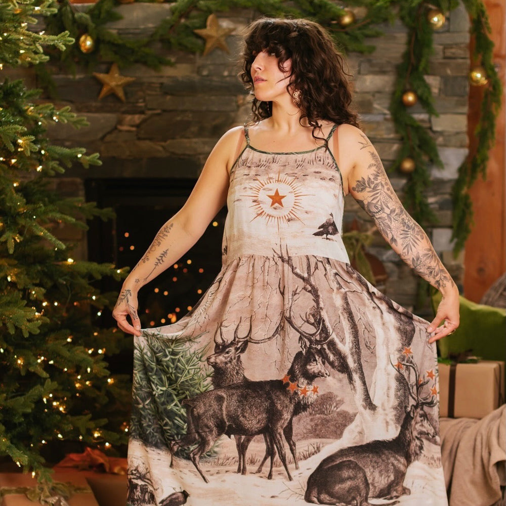 
                  
                    Model wearing a bamboo viscose maxi slip dress with Victorian-era images from holiday greeting cards — including reindeer in the snow, a little fir tree, golden stars, and traditional plaid trim - Market of Stars
                  
                