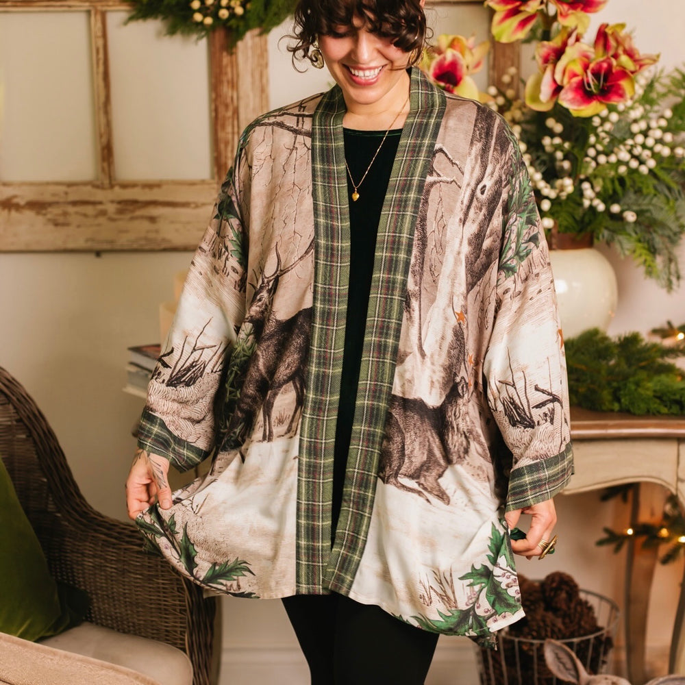 
                  
                    Model wearing a bamboo viscose mid-length duster with Victorian-era images from holiday greeting cards — including reindeer in the snow, a little fir tree, golden stars, and traditional plaid trim - Market of Stars
                  
                