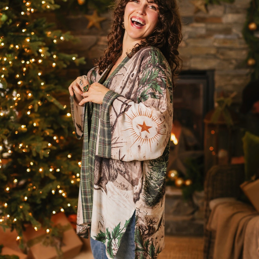 
                  
                    Model wearing a bamboo viscose mid-length duster with Victorian-era images from holiday greeting cards — including reindeer in the snow, a little fir tree, golden stars, and traditional plaid trim - Market of Stars
                  
                