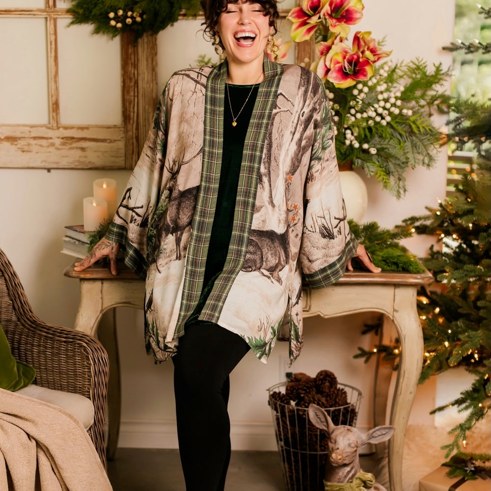 
                  
                    Model wearing a bamboo viscose mid-length duster with Victorian-era images from holiday greeting cards — including reindeer in the snow, a little fir tree, golden stars, and traditional plaid trim - Market of Stars
                  
                