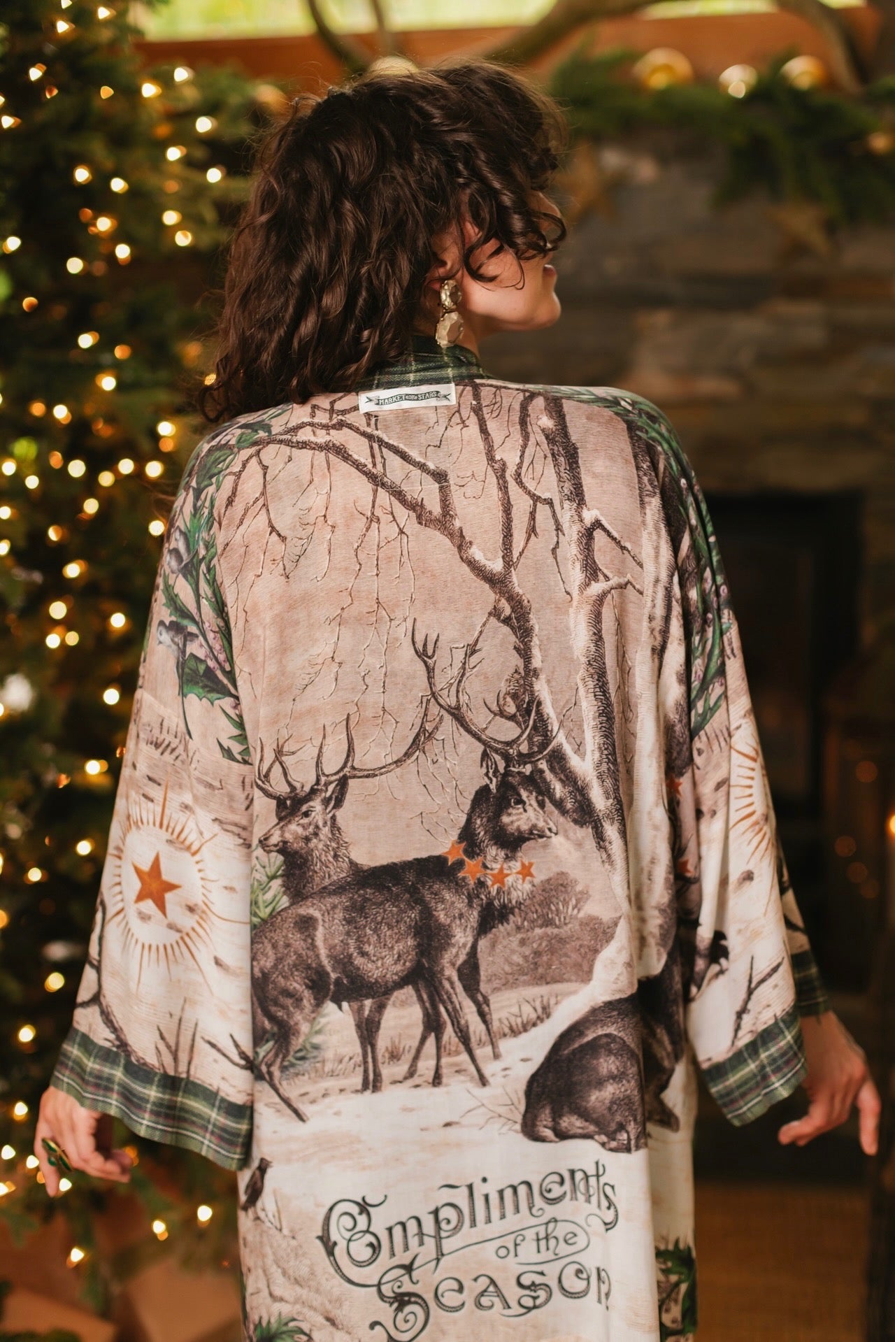 Model wearing a bamboo viscose mid-length duster with Victorian-era images from holiday greeting cards — including reindeer in the snow, a little fir tree, golden stars, and traditional plaid trim - Market of Stars