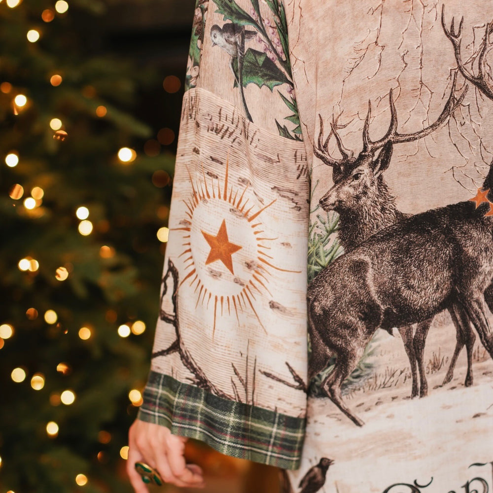 
                  
                    Model wearing a bamboo viscose mid-length duster with Victorian-era images from holiday greeting cards — including reindeer in the snow, a little fir tree, golden stars, and traditional plaid trim - Market of Stars
                  
                