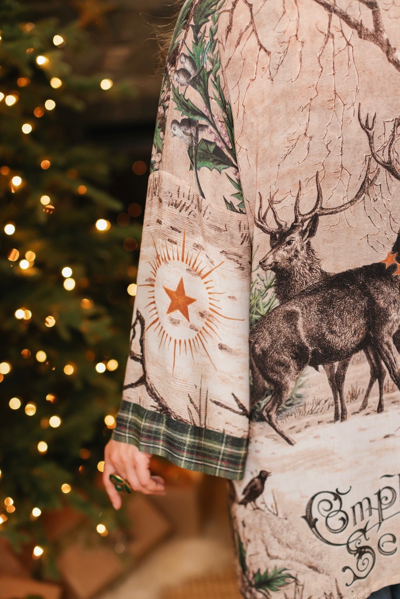Model wearing a bamboo viscose mid-length duster with Victorian-era images from holiday greeting cards — including reindeer in the snow, a little fir tree, golden stars, and traditional plaid trim - Market of Stars