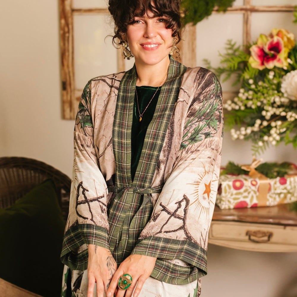 
                  
                    Model wearing a bamboo viscose mid-length duster with Victorian-era images from holiday greeting cards — including reindeer in the snow, a little fir tree, golden stars, and traditional plaid trim - Market of Stars
                  
                