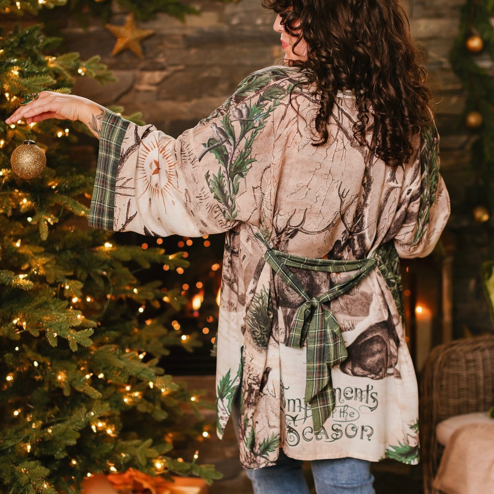 
                  
                    Model wearing a bamboo viscose mid-length duster with Victorian-era images from holiday greeting cards — including reindeer in the snow, a little fir tree, golden stars, and traditional plaid trim - Market of Stars
                  
                