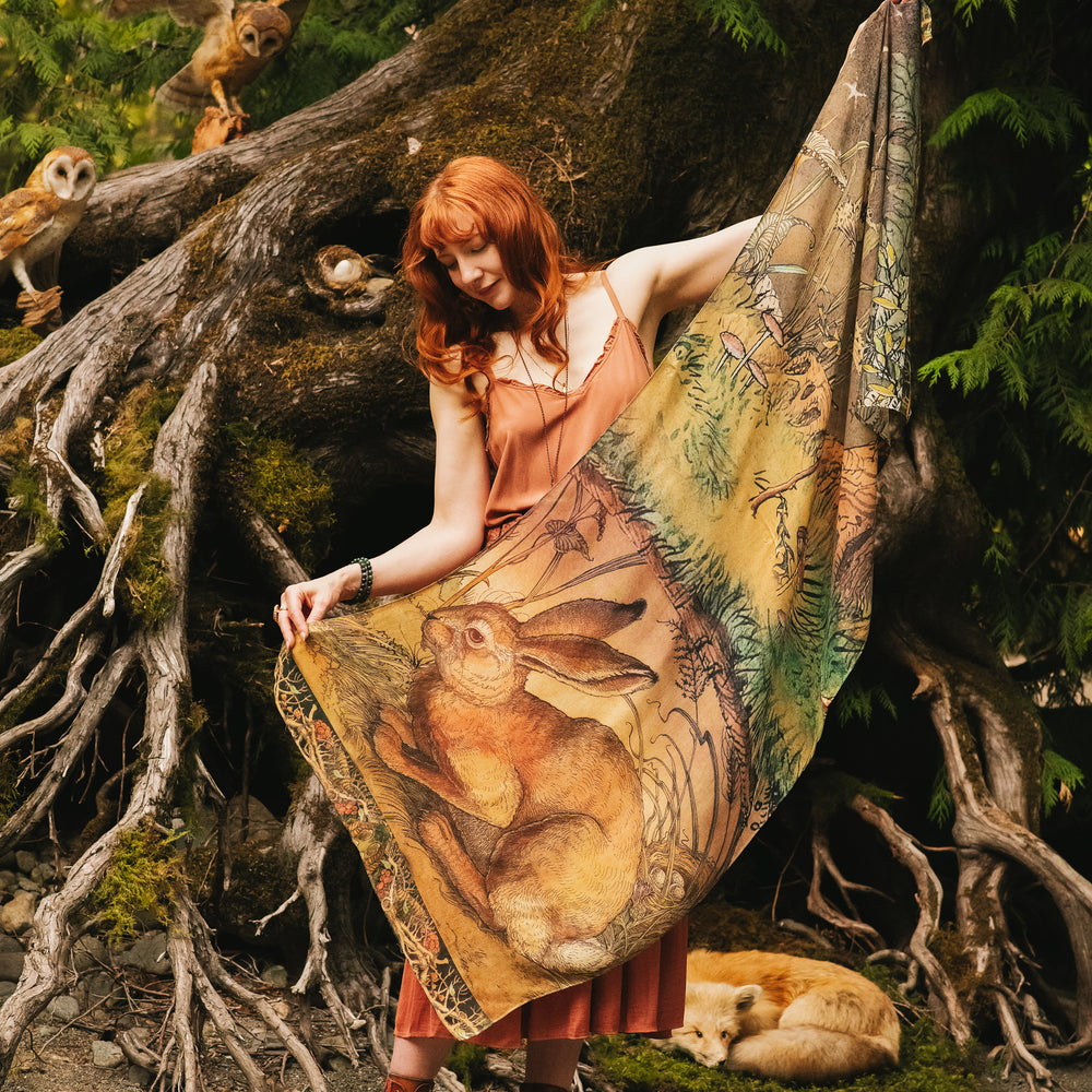 Model wearing a bamboo-viscose scarf where a noble rabbit rests deep within an underground burrow, surrounded by the warmth and safety of the earth. Created in collaboration with Charles van Sandwyck - Market of Stars
